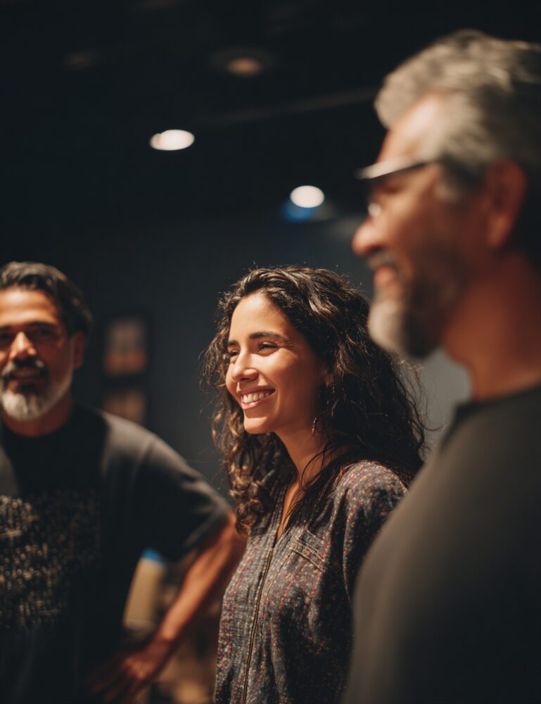 Smiling woman with curly hair stands between two men, all looking engaged in conversation.