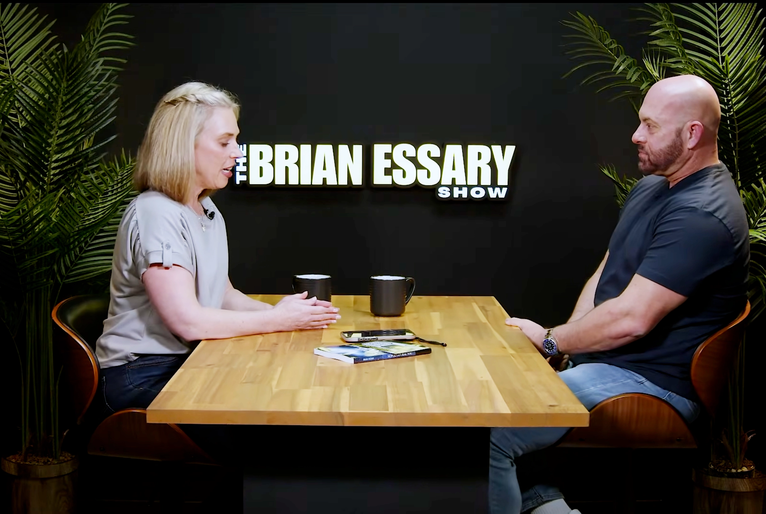 ddrd Brian Essary Show interview: Woman and bald man at table with mugs and book.